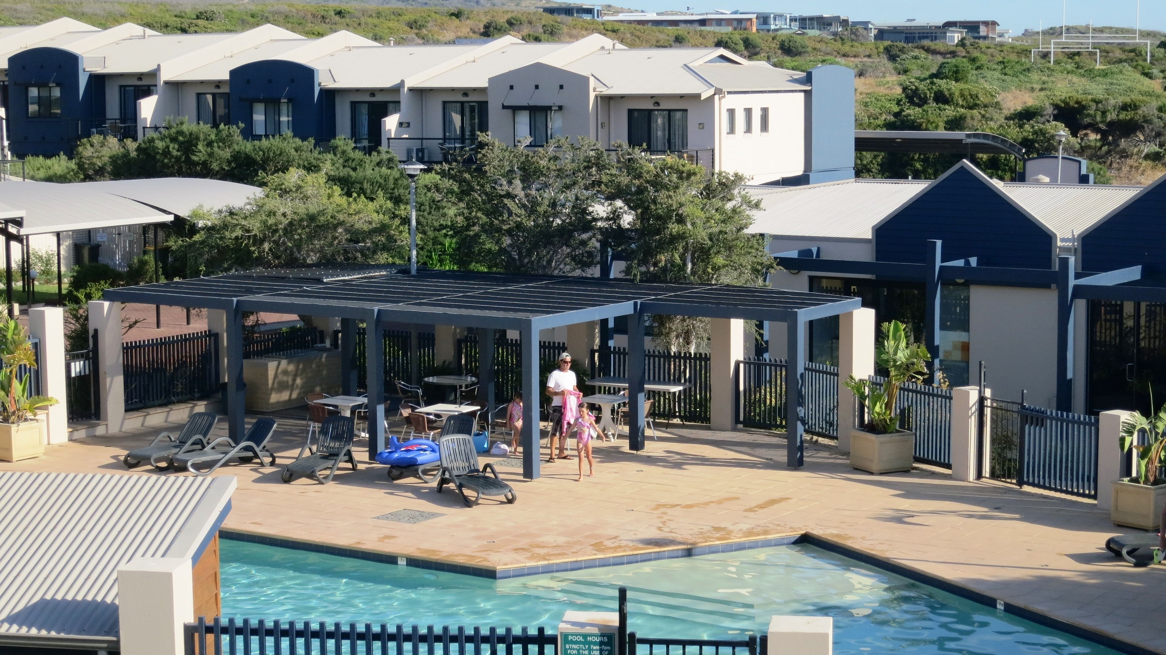 A pool area with a covered seating area, lounge chairs, and a swimming pool.