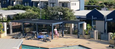 A pool area with a covered seating area, lounge chairs, and a swimming pool.