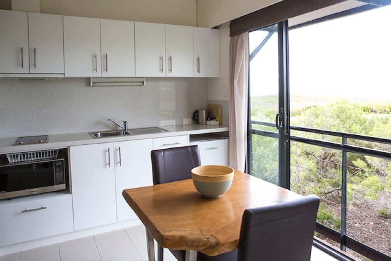 Een moderne keuken met witte kasten, een houten tafel en een groot raam met uitzicht op groen.