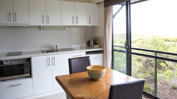 A modern kitchen with white cabinets, a wooden table, and a large window offering a view of greenery.