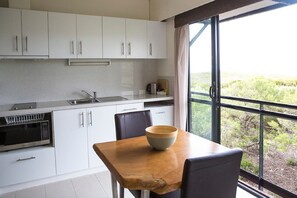 A modern kitchen with white cabinets, a wooden table, and a large window offering a view of greenery.