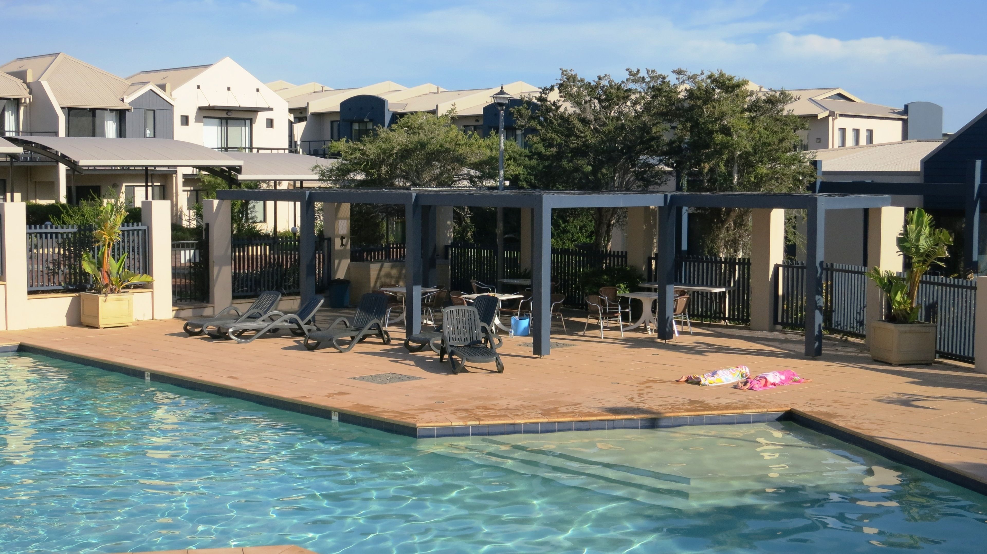 A swimming pool area with lounge chairs and a covered seating area.