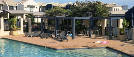 A swimming pool area with lounge chairs and a covered seating area.