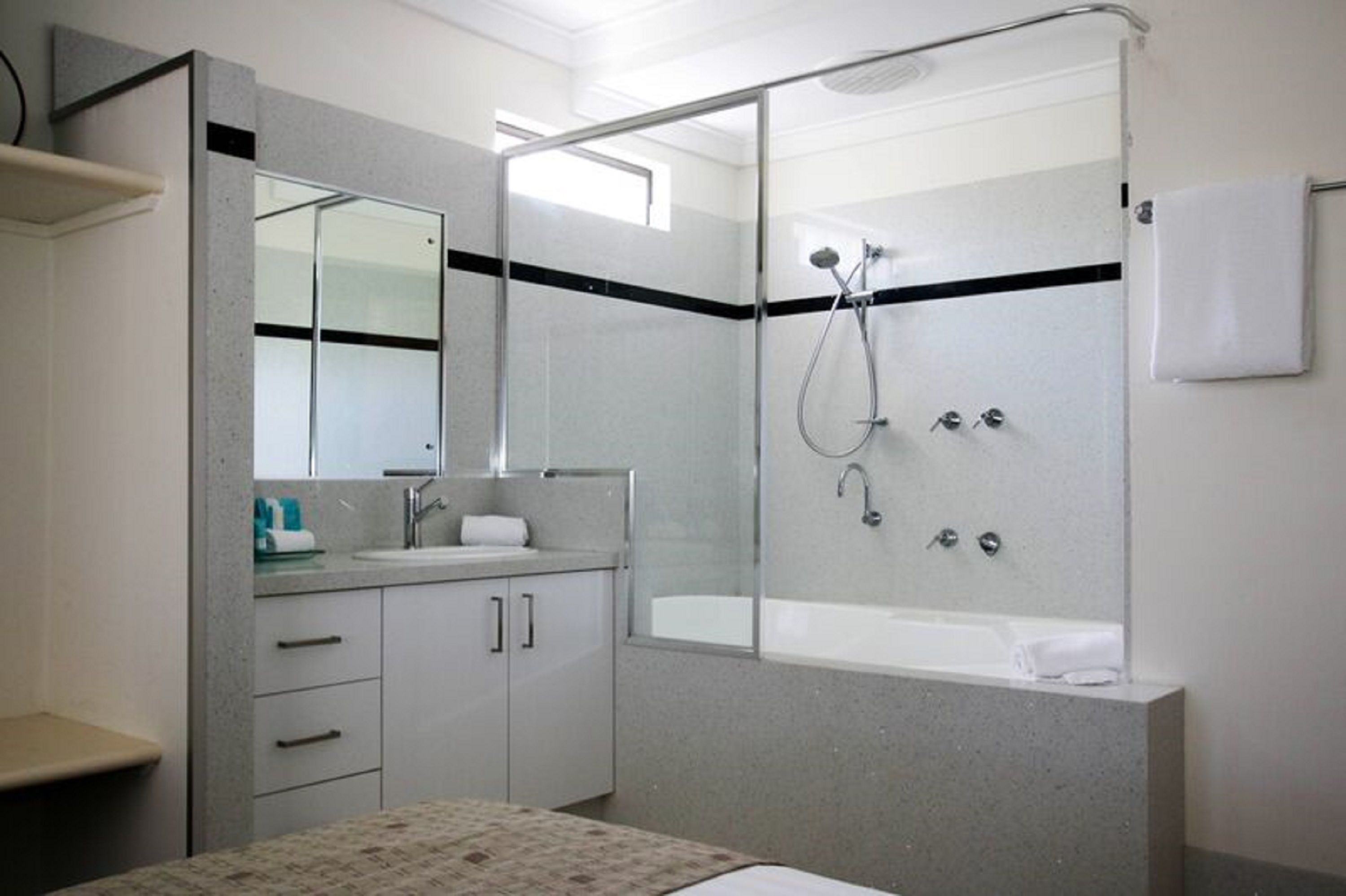 Een moderne badkamer met een douche in een glazen cabine, een grote spiegel en een witte wastafel.