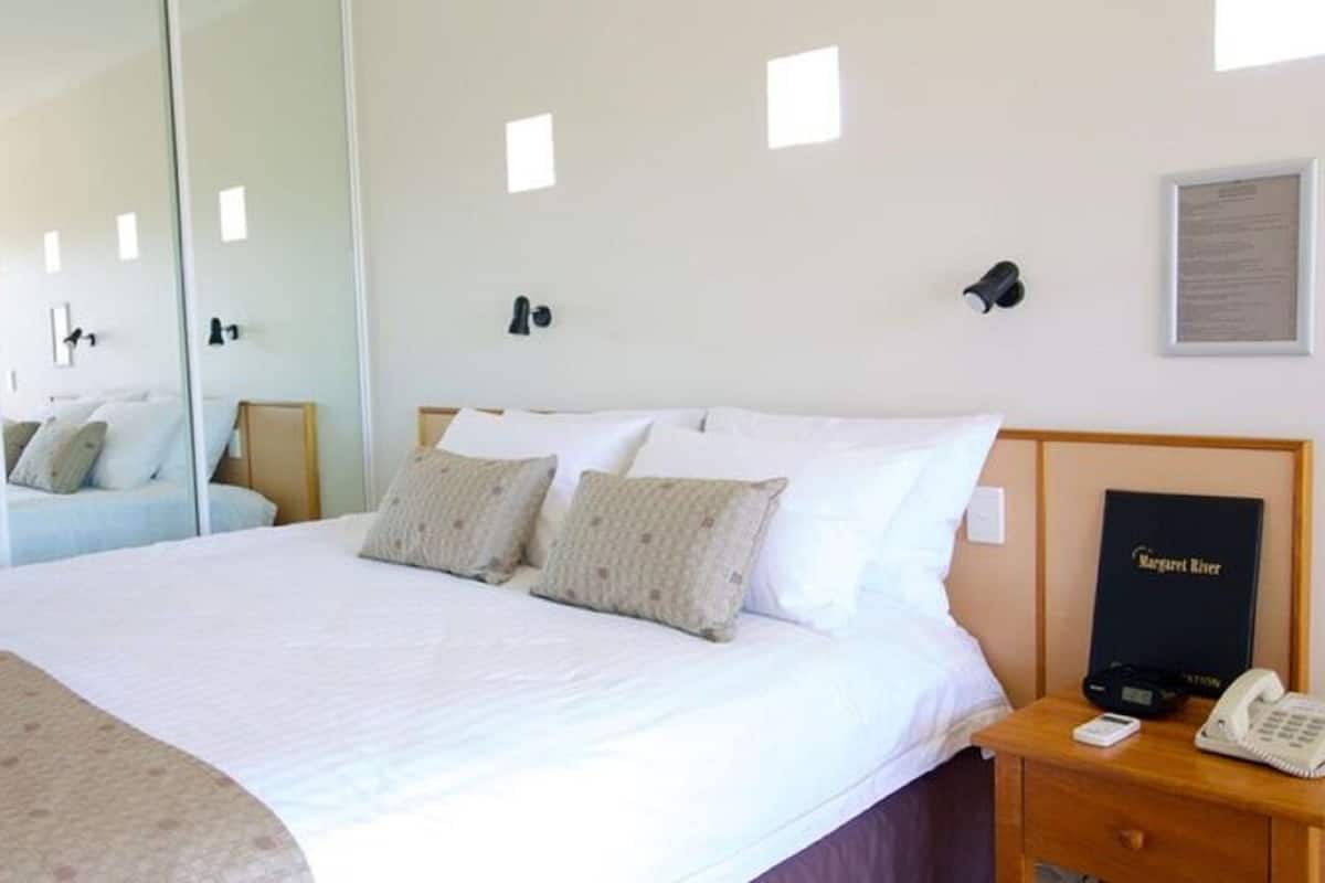 Ein Hotelzimmer mit einem großen Bett, einem Nachttisch mit Telefon und Buch, einem Spiegel und einem gerahmten Zertifikat an der Wand.