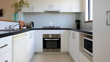 A modern kitchen with white cabinets, a black countertop, a built-in oven, and a microwave.