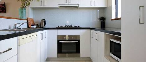 A modern kitchen with white cabinets, a black countertop, a built-in oven, and a microwave.