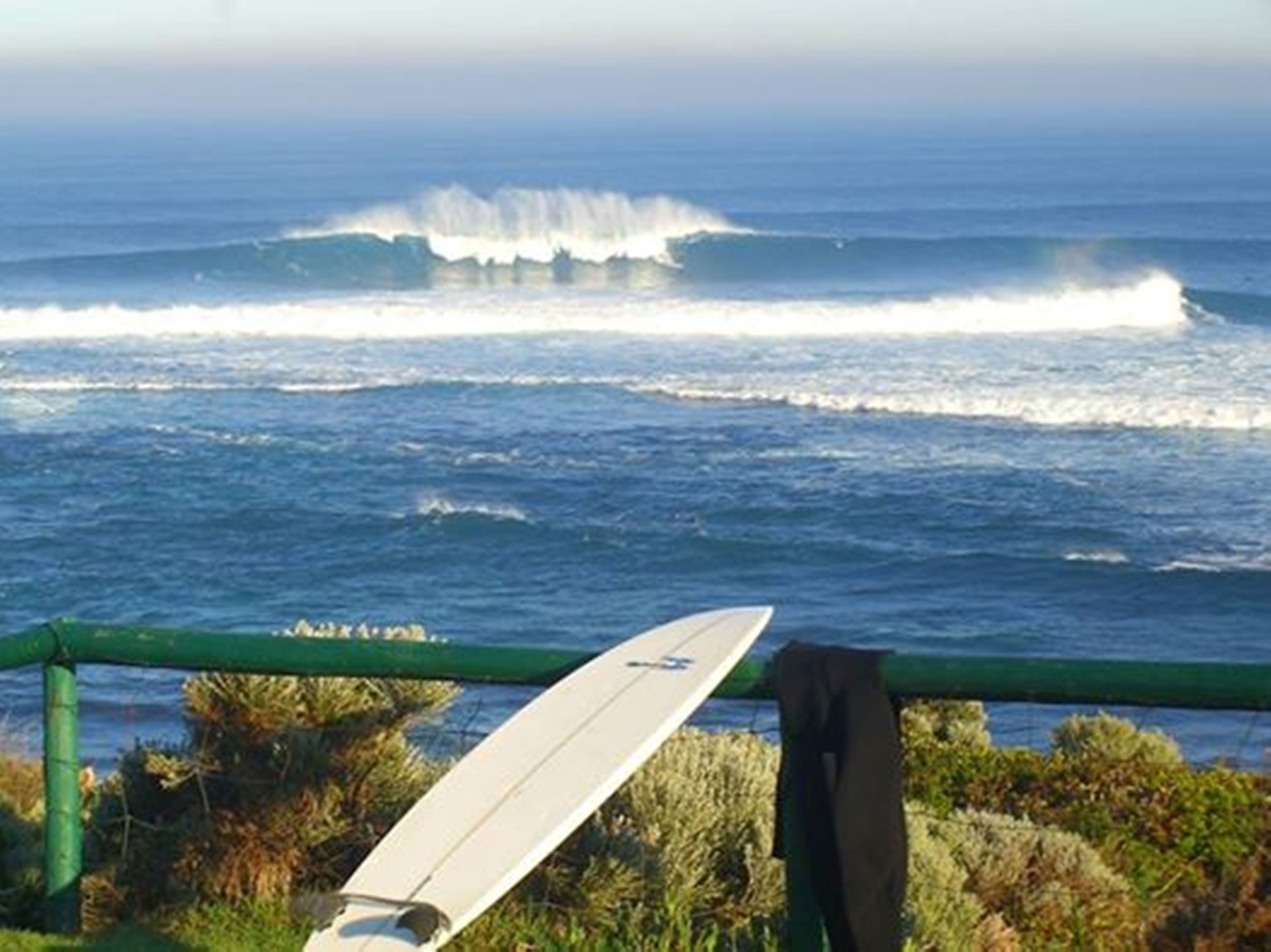 Una taula de surf apujada contra una barana amb vista a onades oceàniques.