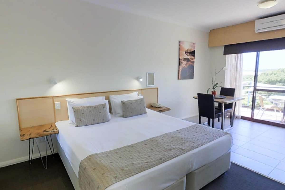Ein Hotelzimmer mit einem großen Bett, einem Schreibtisch mit Stuhl und Blick ins Freie.