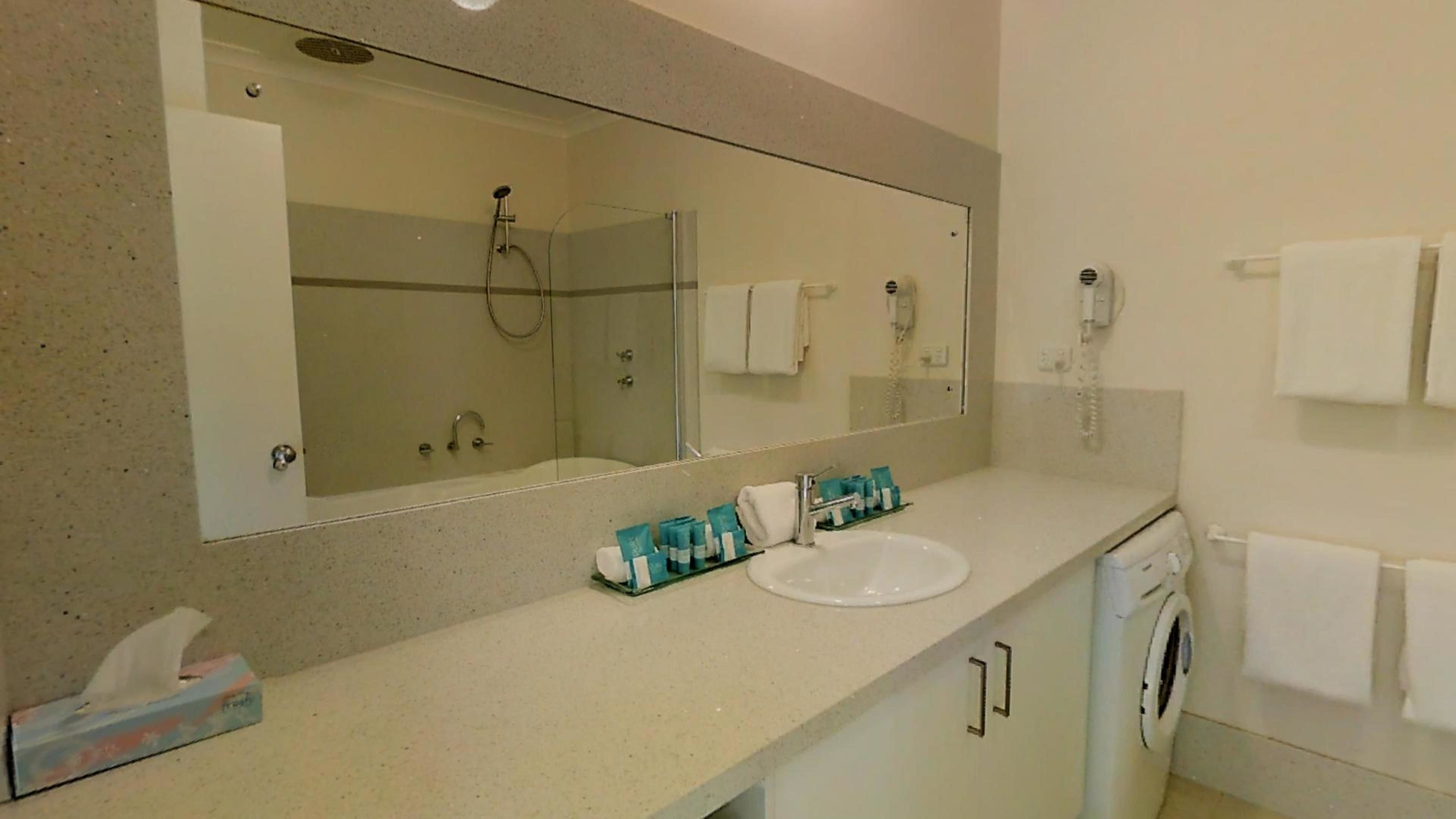 A bathroom with a large mirror, a sink, a shower, and a washing machine.