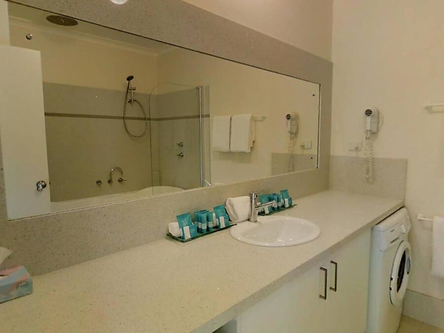 A bathroom with a large mirror, a sink, a shower, and a washing machine.