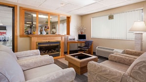 A living room with beige patterned sofas, a wooden coffee table, a fireplace, a computer desk, and a large window with blinds. - Baymont by Wyndham Midland (Midland)