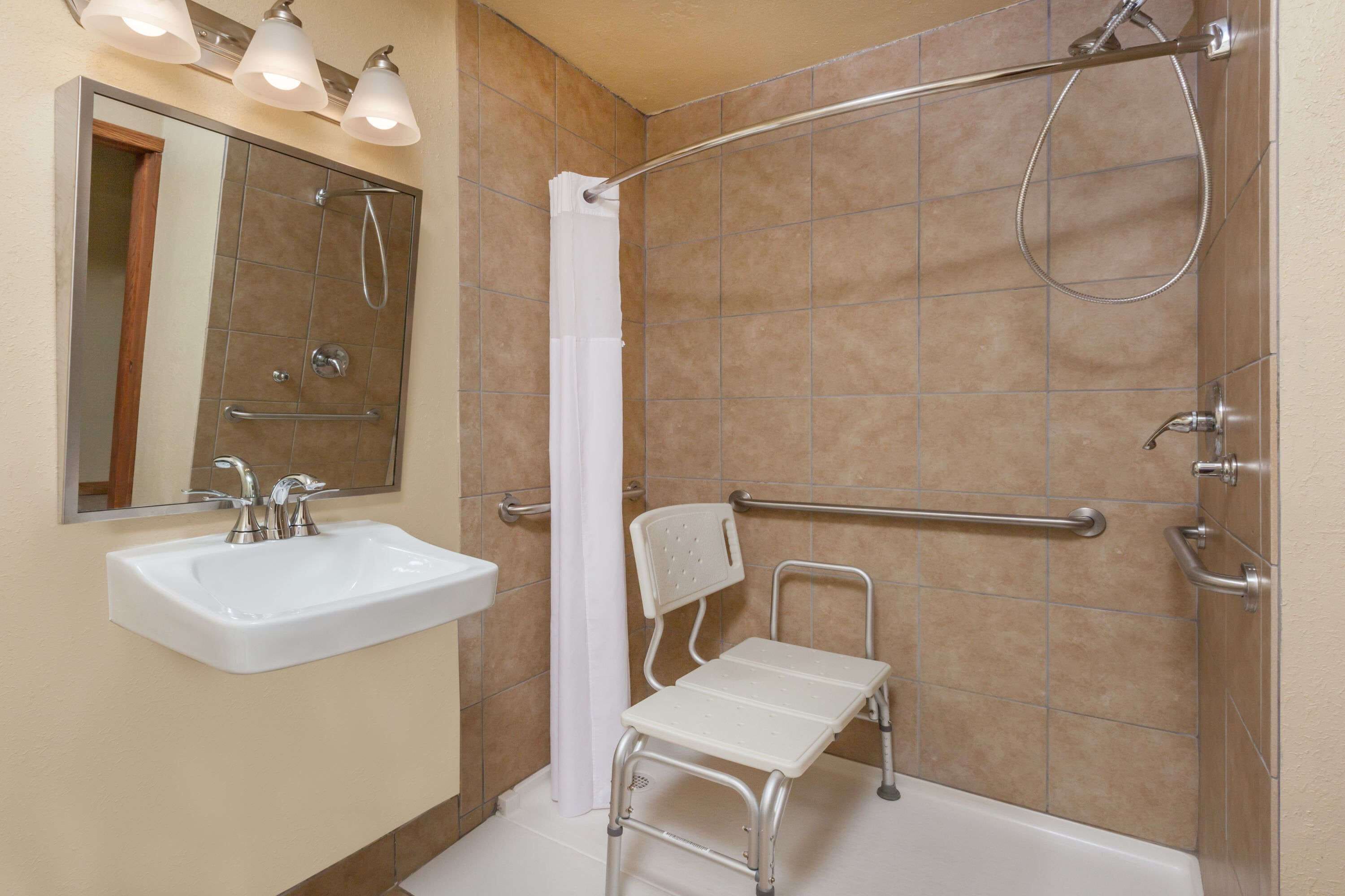 A bathroom with a white sink, a shower with a grab bar, and a wheelchair-accessible bench.