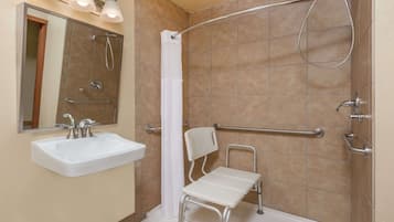 A bathroom with a white sink, a shower with a grab bar, and a wheelchair-accessible bench.