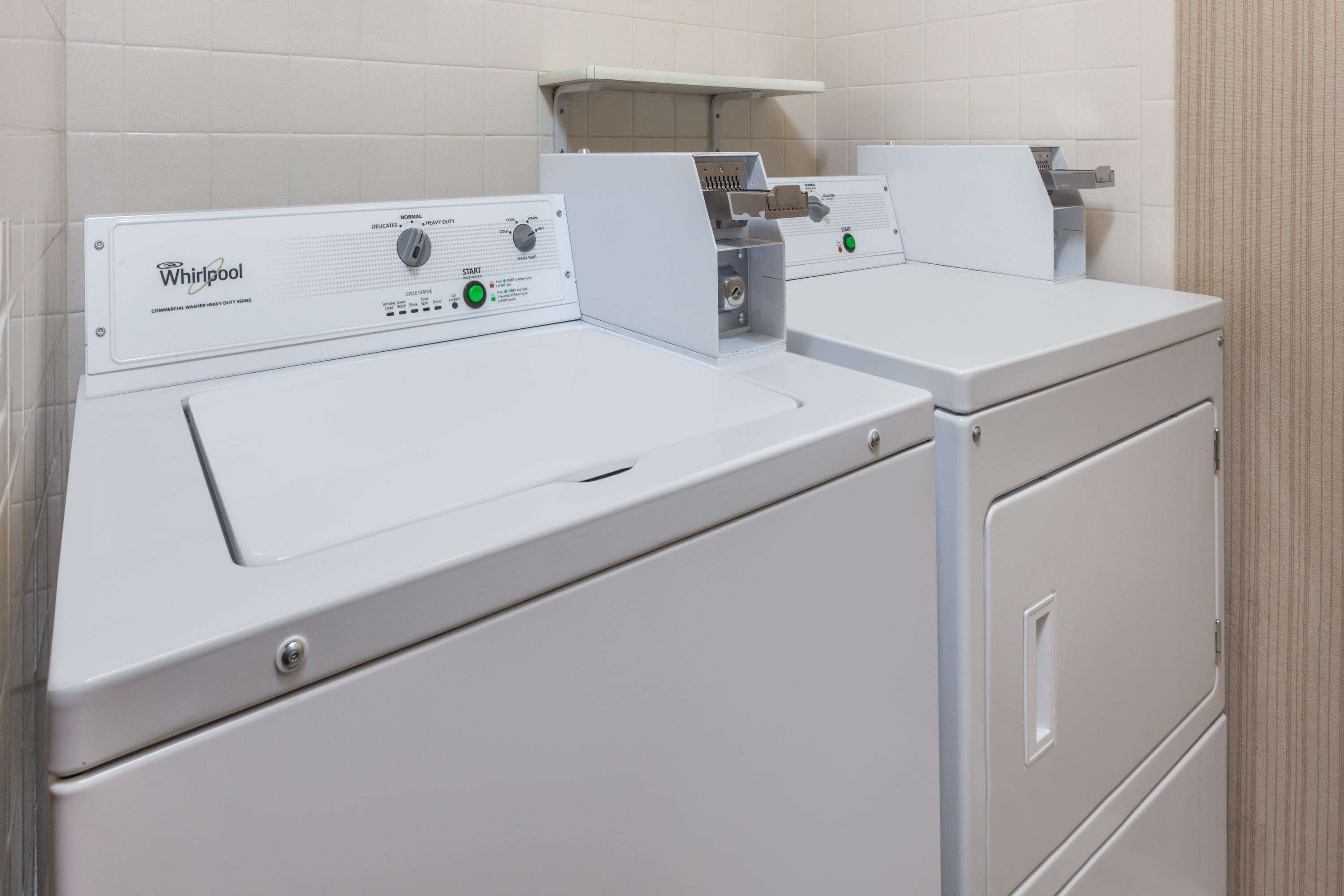 Two Whirlpool front-loading washing machines in a laundry area with tiled walls and a wooden panel above.