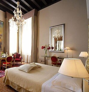 A hotel room with a bed, a desk, a chair, a lamp, and a chandelier. - Liassidi Palace Hotel (Venice)