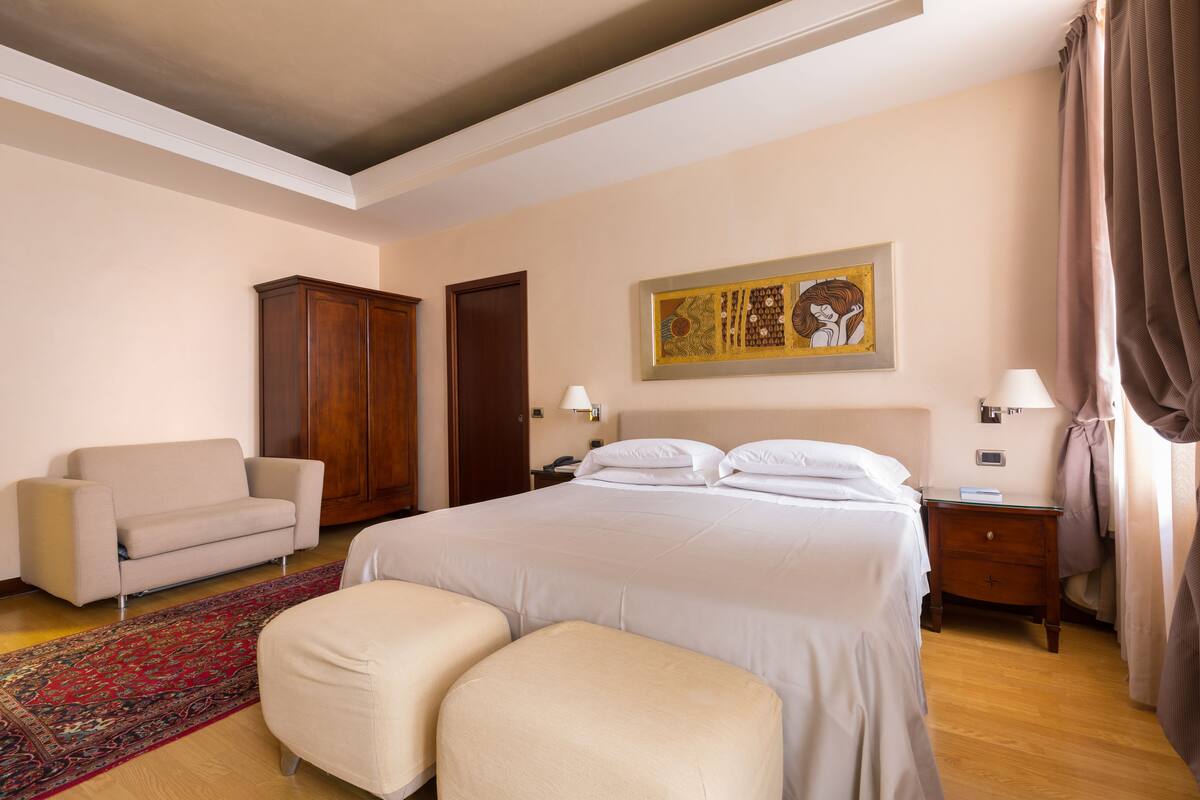 Ein Hotelzimmer mit einem großen Bett, einem Schlafsofa, einem Holzschrank, einem Nachttisch und einem Gemälde an der Wand.