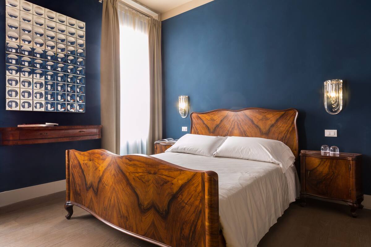 Ein Schlafzimmer mit einem hölzernen Bett, zwei Nachttischen, einer Wandleuchte und einem großen Spiegel.