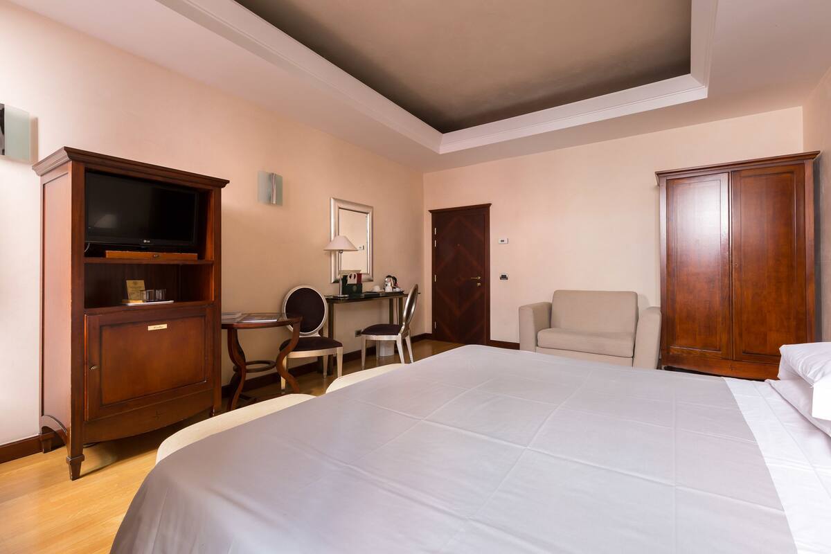 Ein Hotelzimmer mit einem großen Bett, einem Schreibtisch mit Stuhl, einem Kleiderschrank und einem Fernseher.