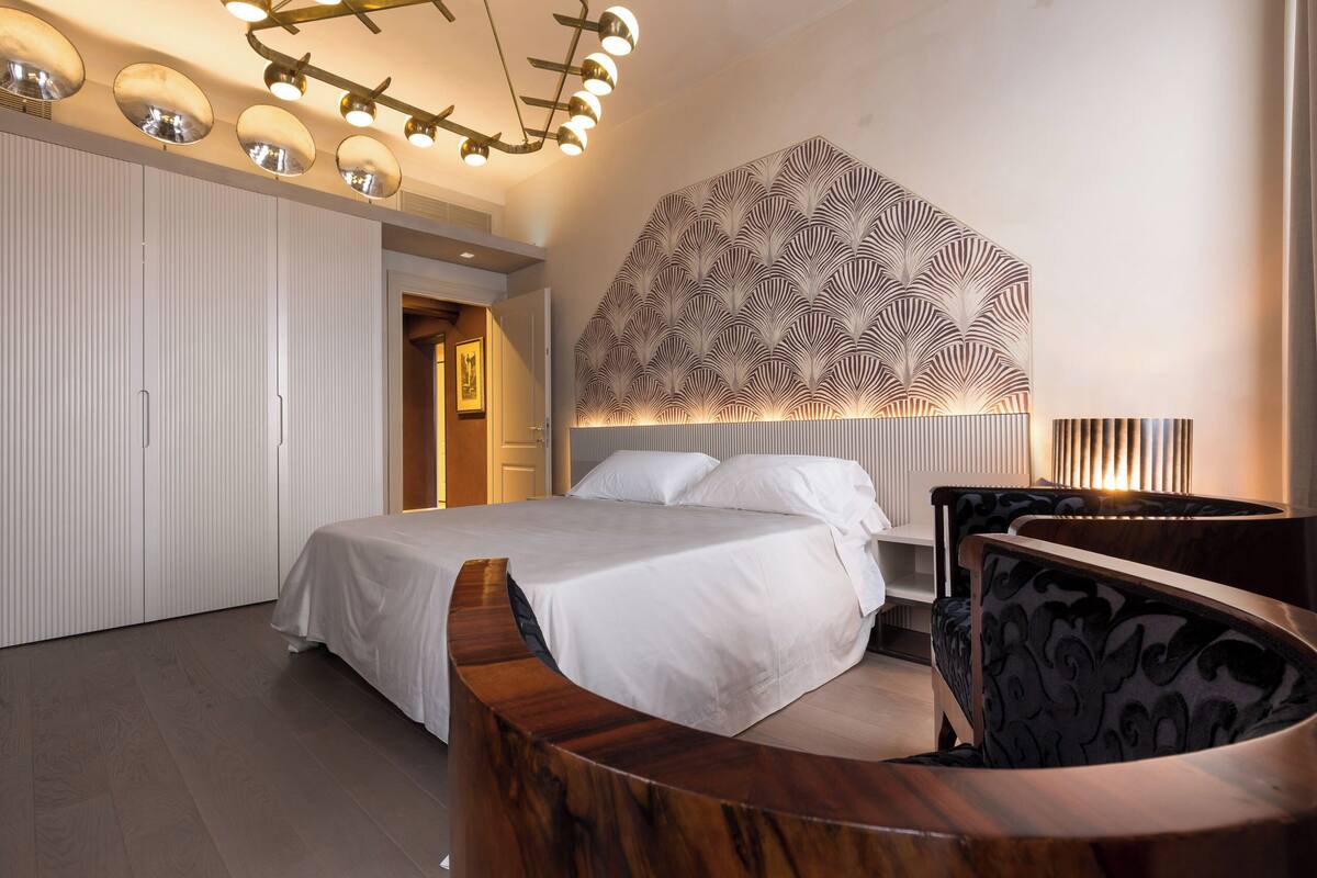 Ein modernes Schlafzimmer mit einem gewölbten Holz-Kopfteil, einem großen Bett, einer Wand mit Muster und einer Deckenleuchte.
