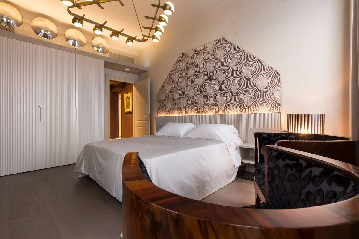 Ein modernes Schlafzimmer mit einem gewölbten Holz-Kopfteil, einem großen Bett, einer Wand mit Muster und einer Deckenleuchte.