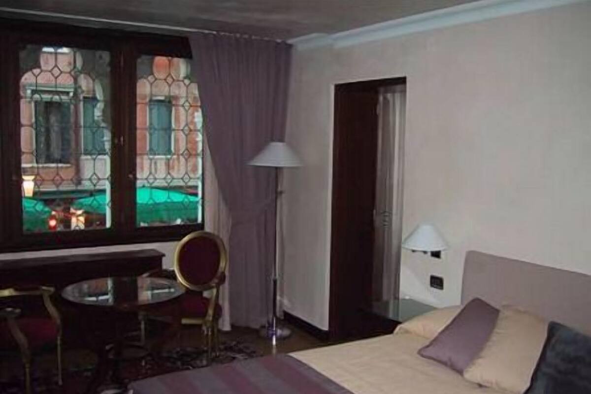 Ein Hotelzimmer mit Bett, Schreibtisch, Stuhl, Fenster mit Vorhängen und Lampe.