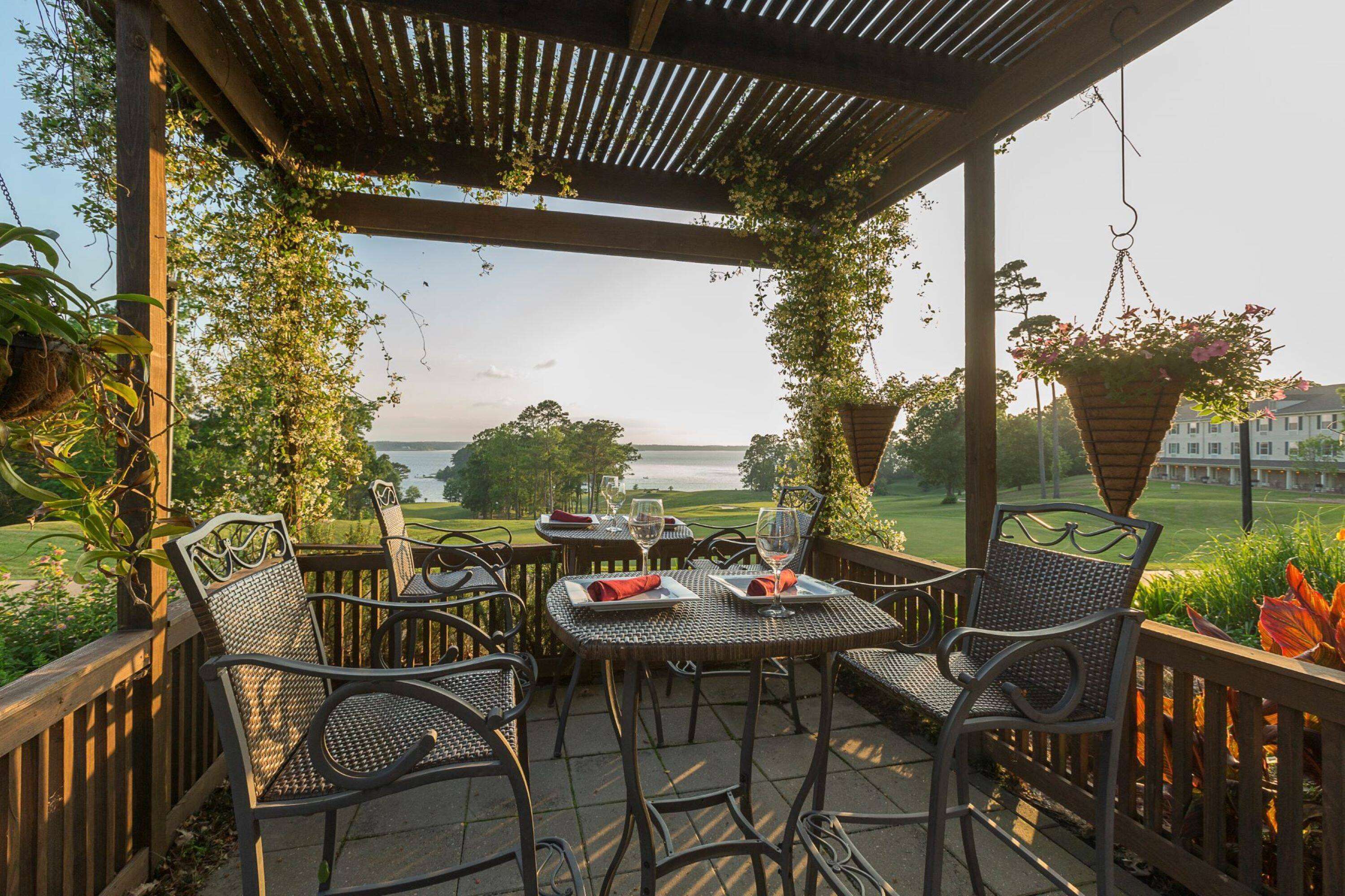 An outdoor patio with wicker chairs and tables, overlooking a golf course and a body of water.