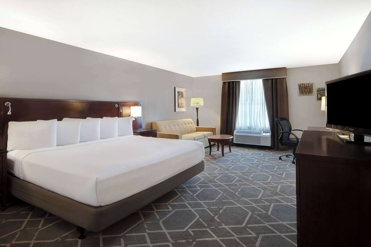A hotel room with a large bed, a sofa, a desk, a TV, and a window with curtains.