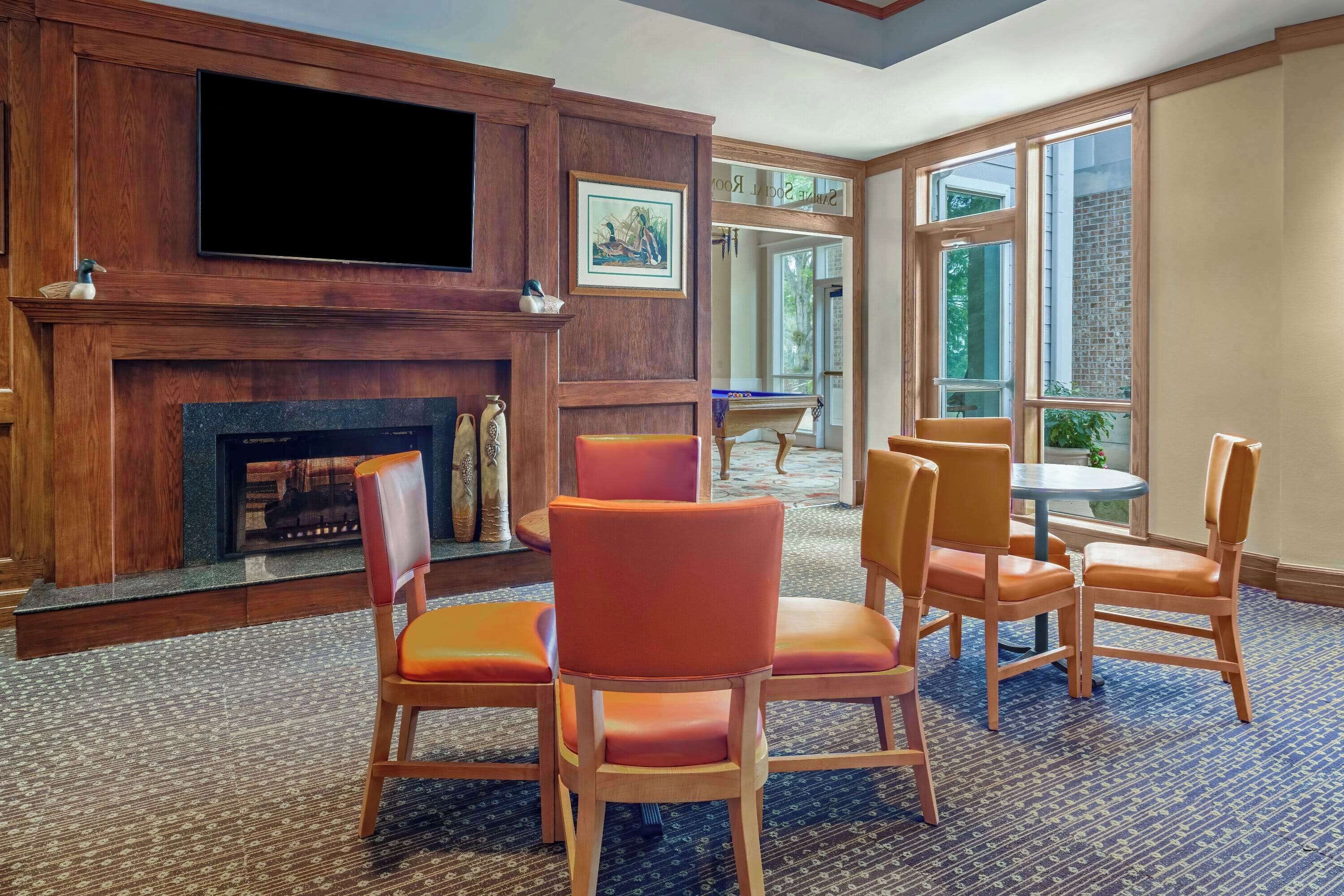 A room with a fireplace, wooden paneling, a television, and orange chairs.