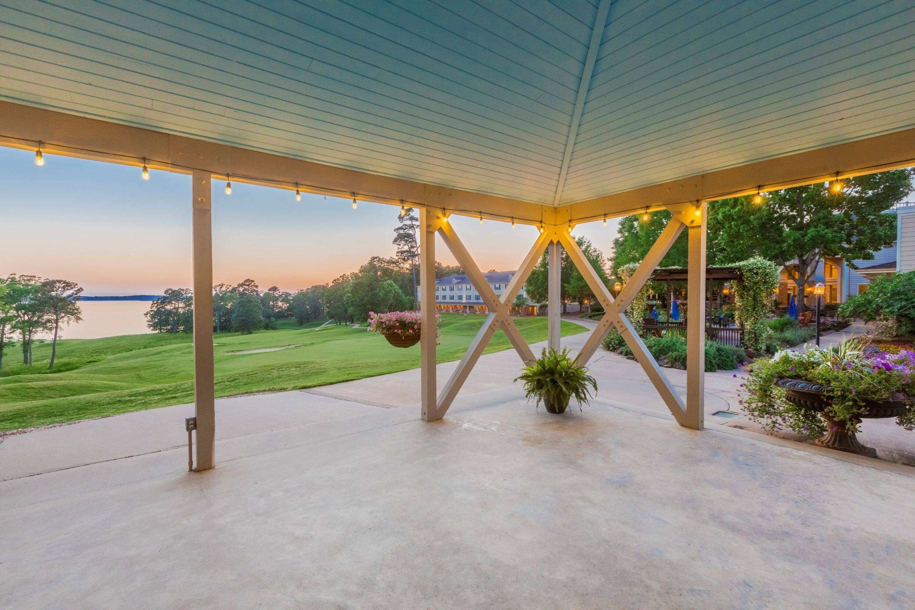 An outdoor patio area with a view of a lake, a covered structure with hanging lights, and potted plants.