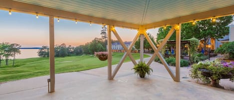 An outdoor patio area with a view of a lake, a covered structure with hanging lights, and potted plants.
