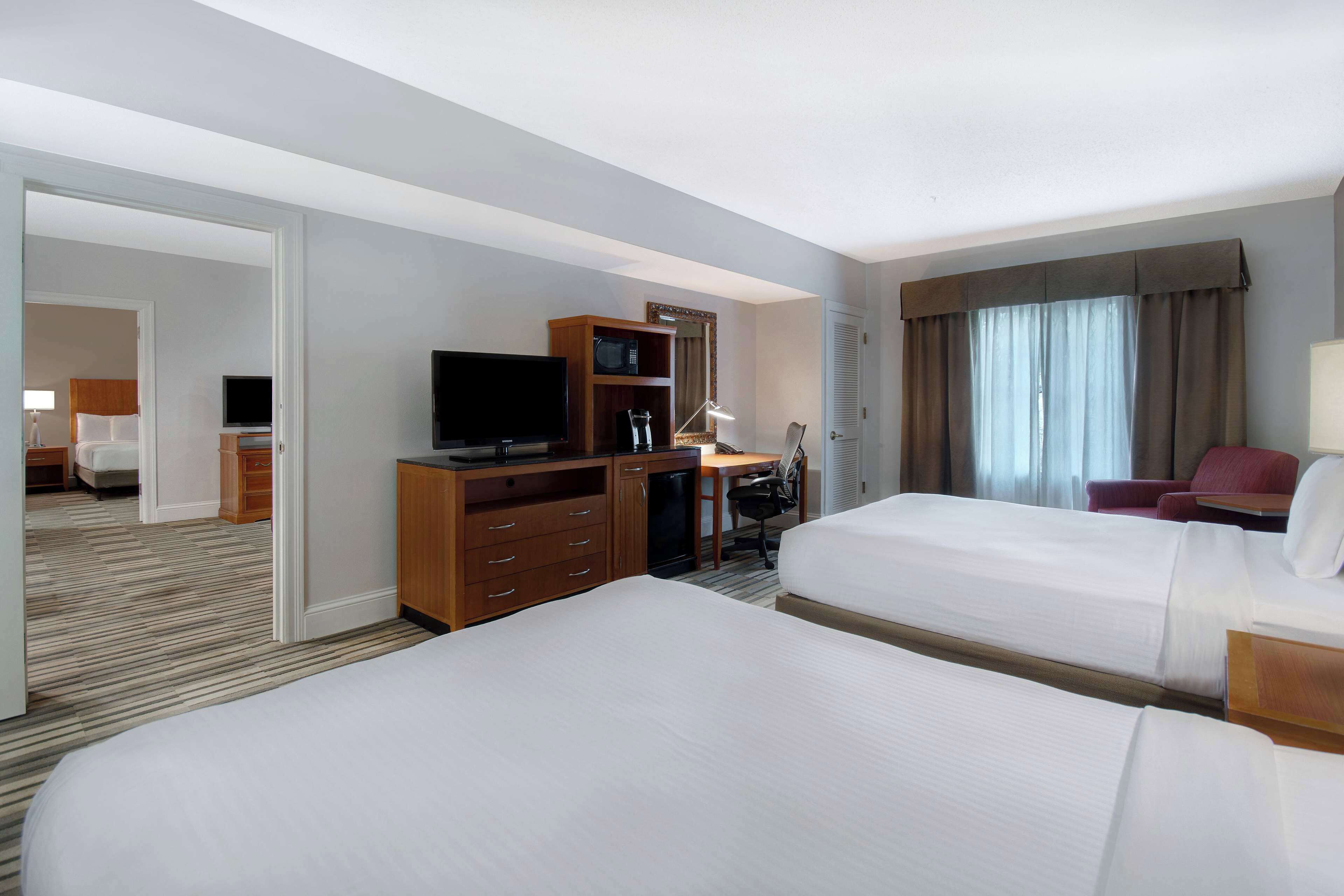 Quarto de hotel com duas camas, uma escrivaninha com cadeira, televisão e minibar.