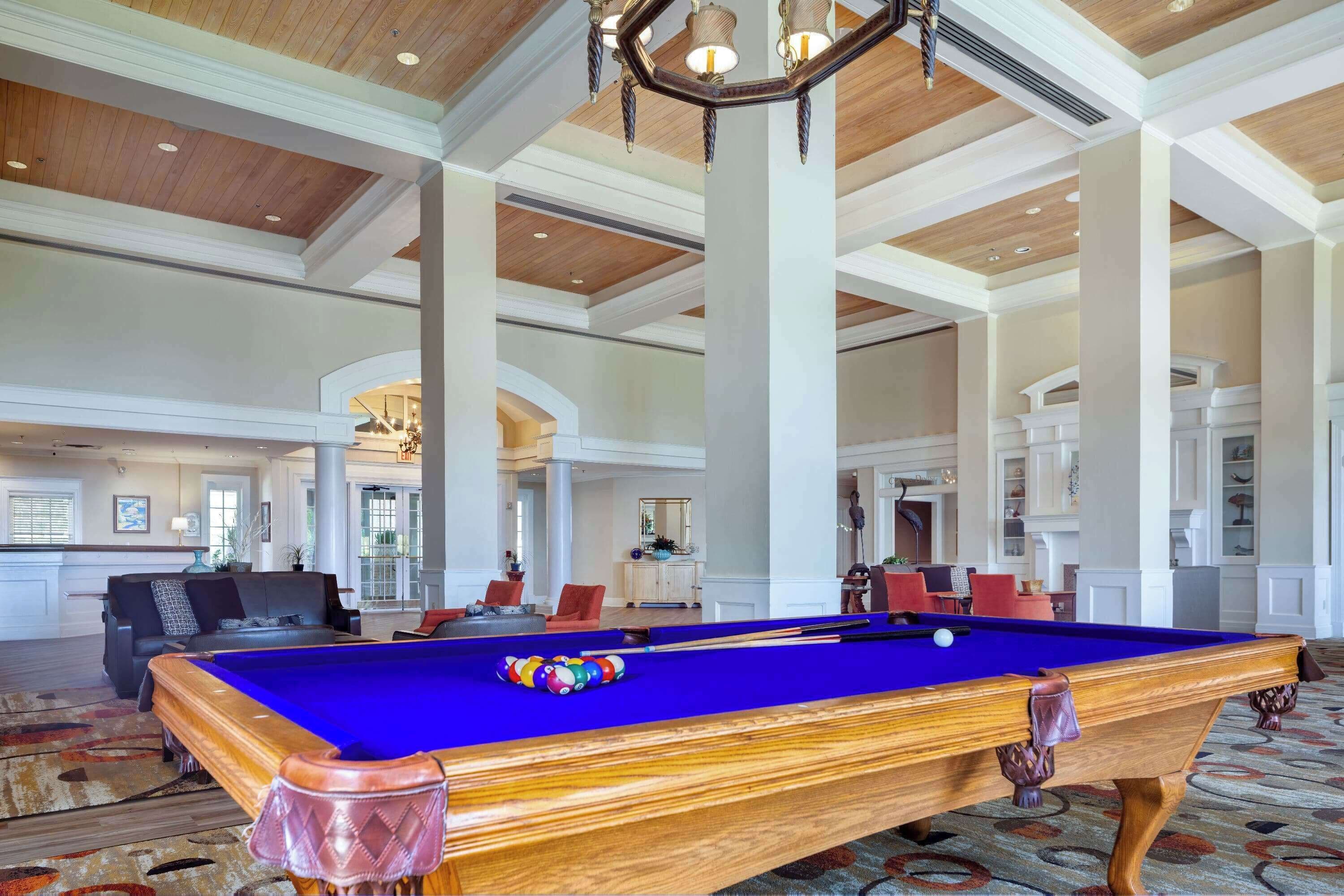 A spacious indoor area with a pool table, comfortable seating, and a high ceiling with wooden beams.