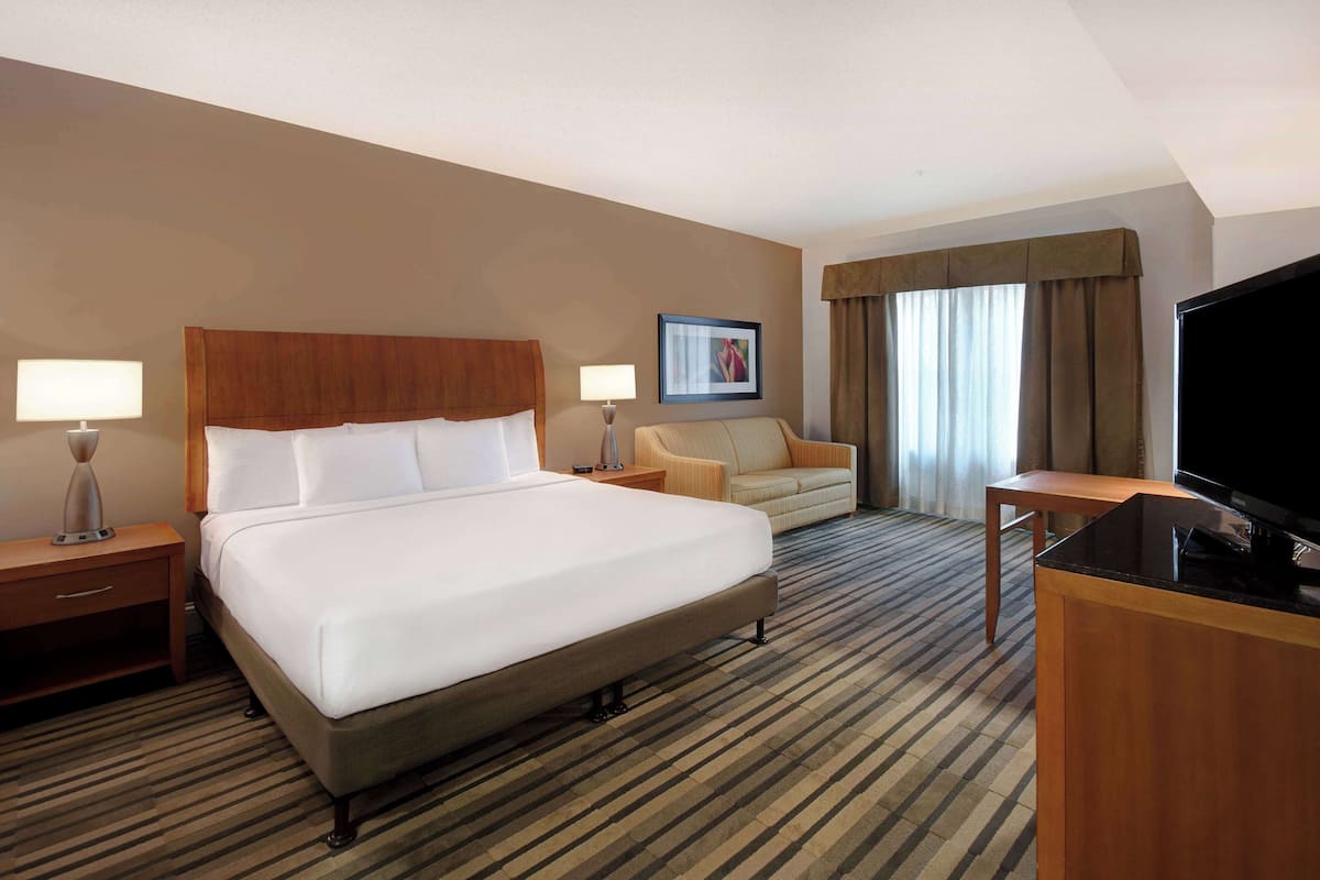 A hotel room with a large bed, a sofa, a TV, and a desk.