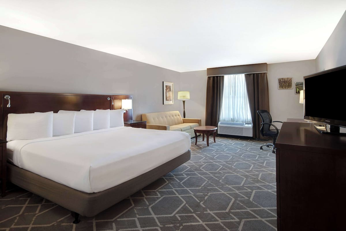 A hotel room with a large bed, a sofa, a desk, a TV, and a window with curtains.