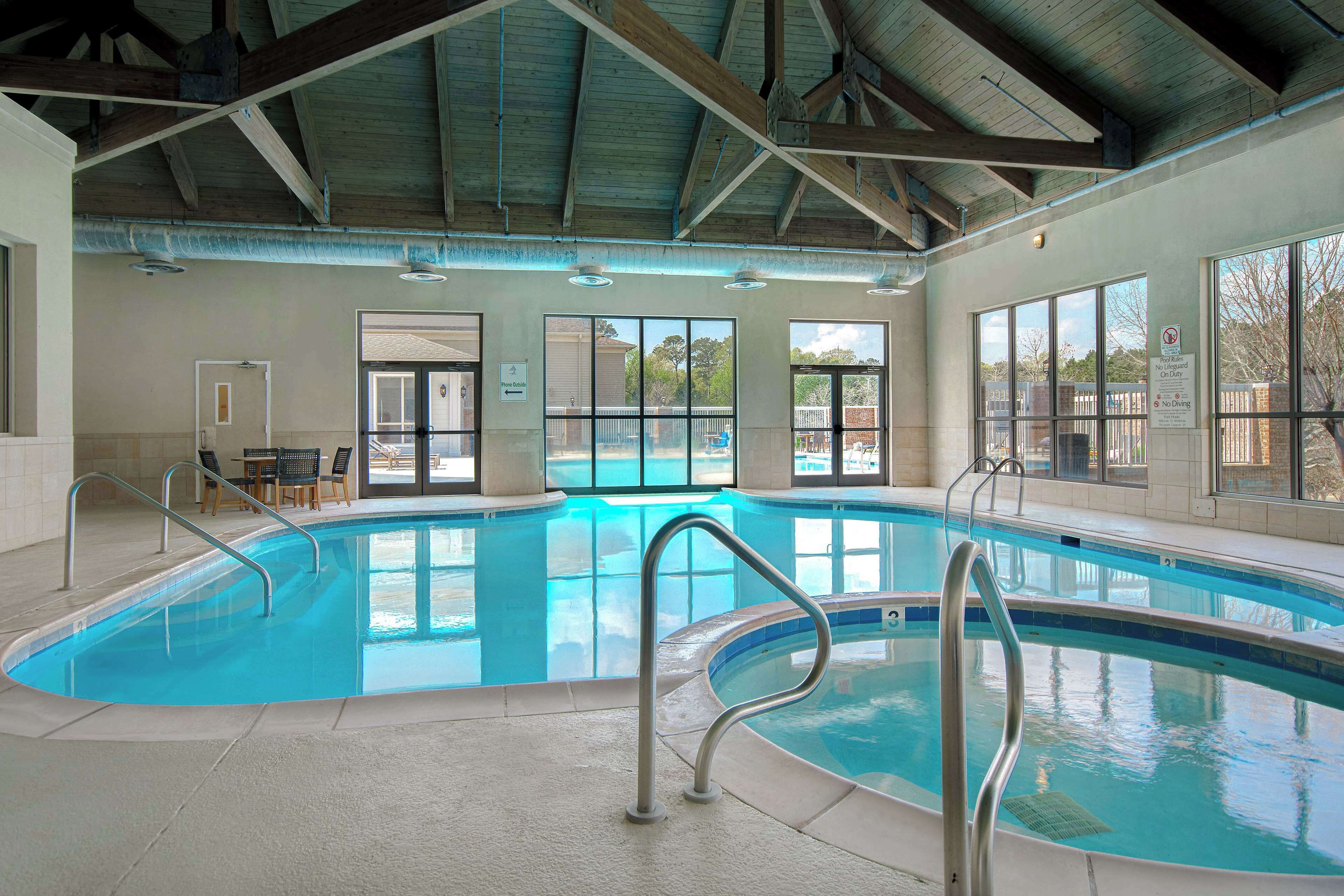 An indoor swimming pool with clear blue water, metal pool ladders, and large windows offering views of the outside.