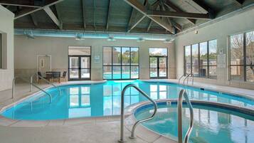 An indoor swimming pool with clear blue water, metal pool ladders, and large windows offering views of the outside.