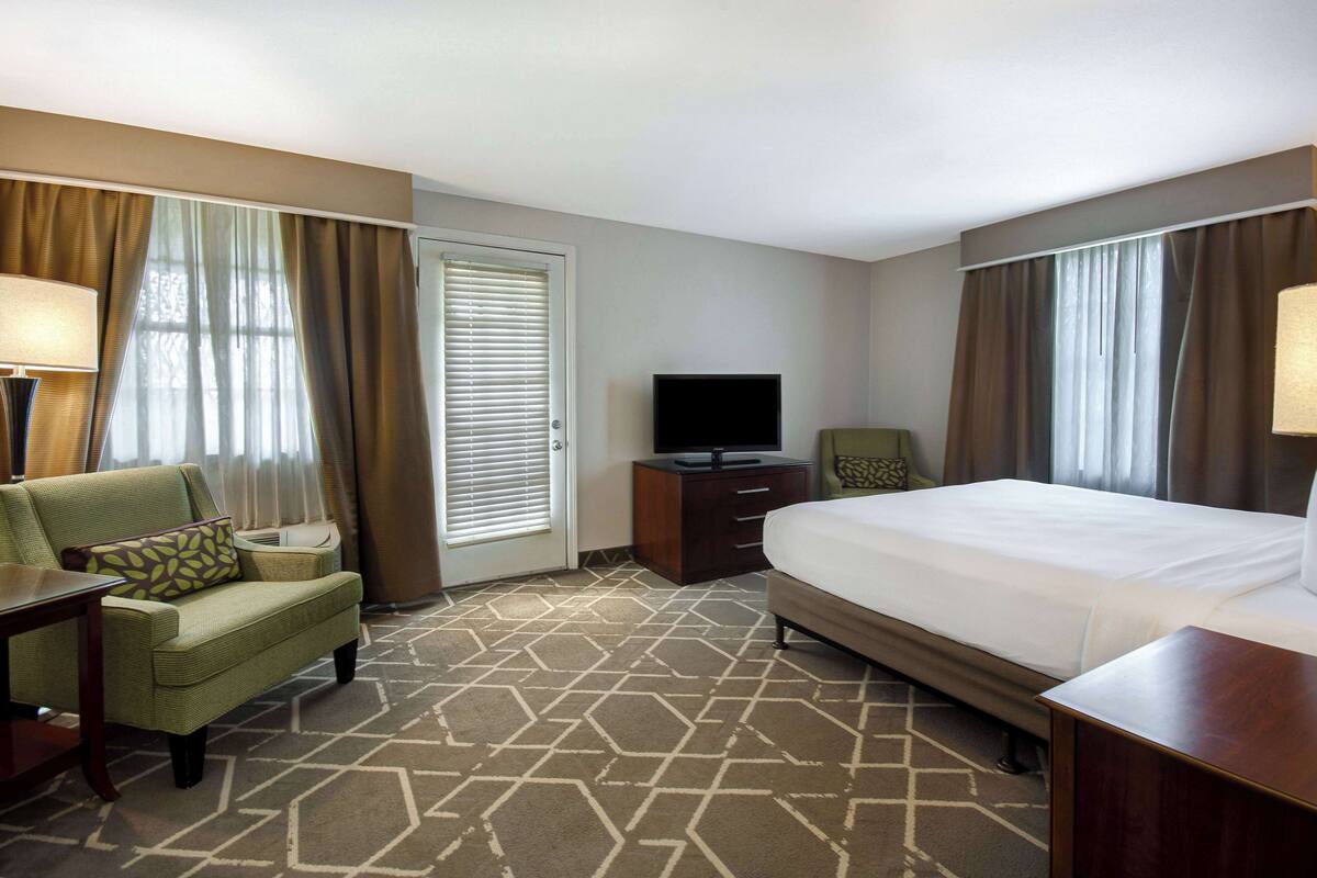 A hotel room with a bed, a chair, a TV, and a desk.