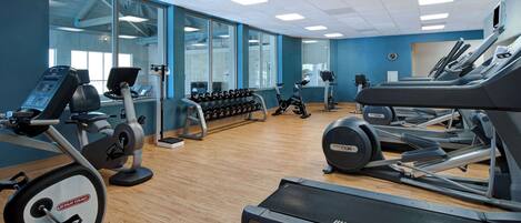 A gym with cardio machines, dumbbells, and a mirror.