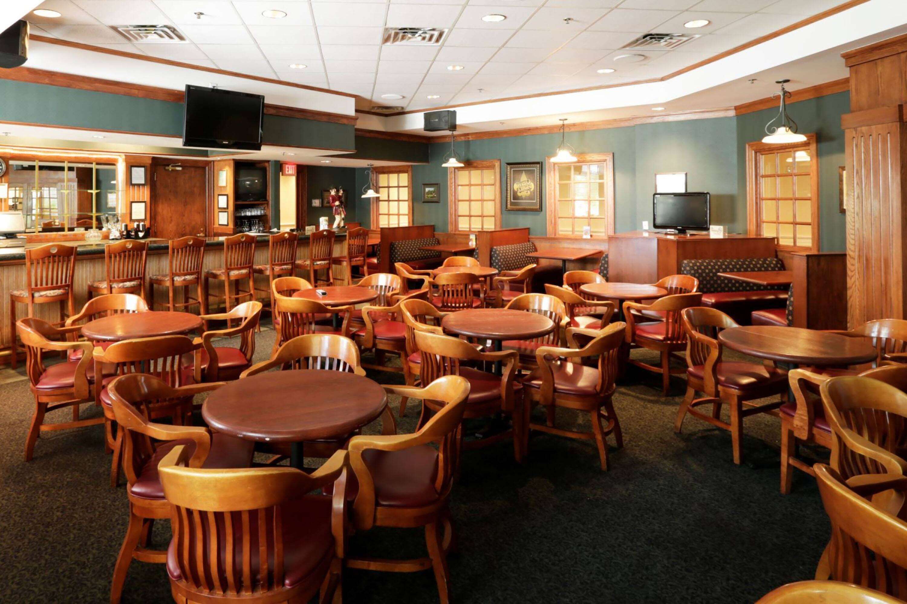 Un restaurant doté de nombreuses tables et chaises en bois, d’un bar et d’un écran de télévision.