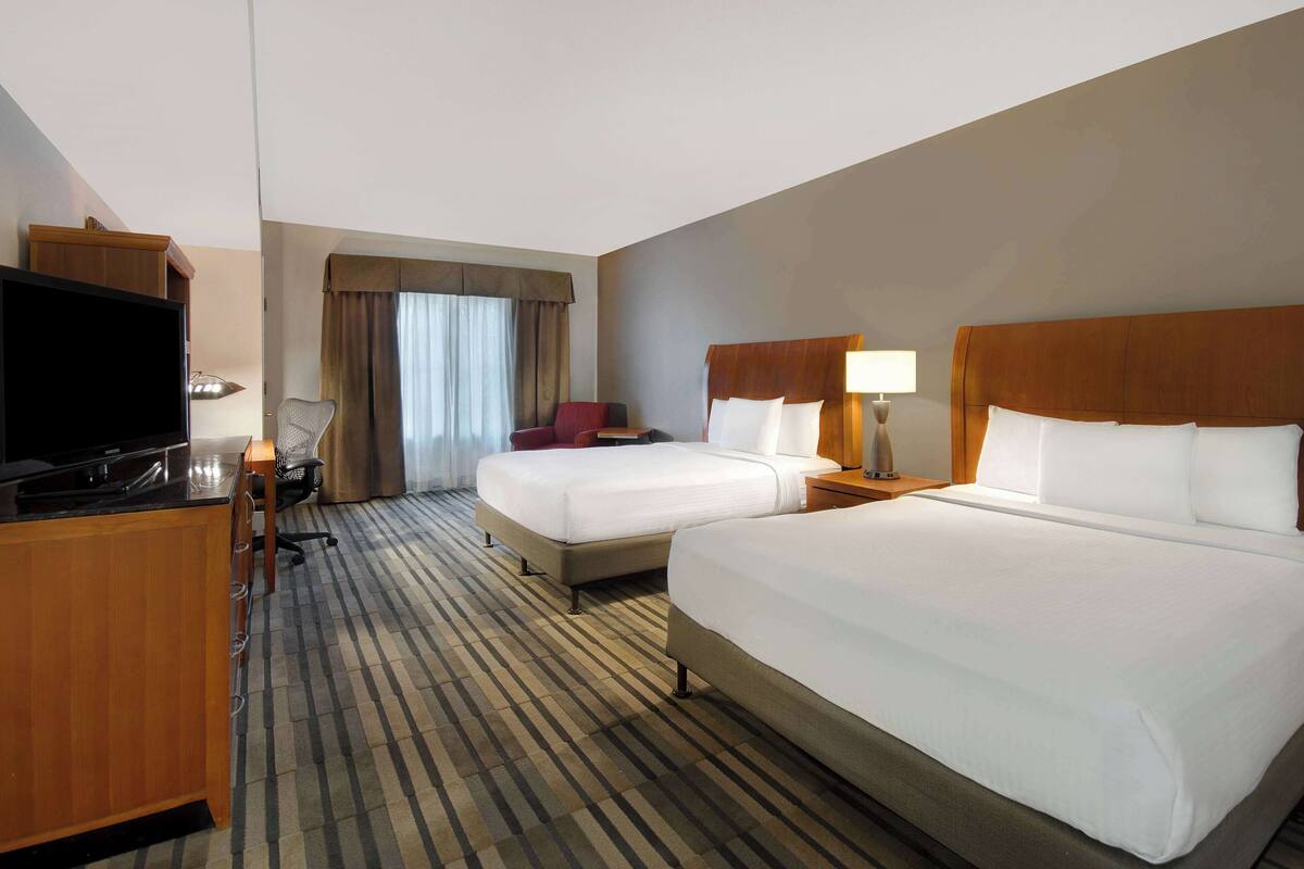 A hotel room with two beds, a desk with a television, and a chair.