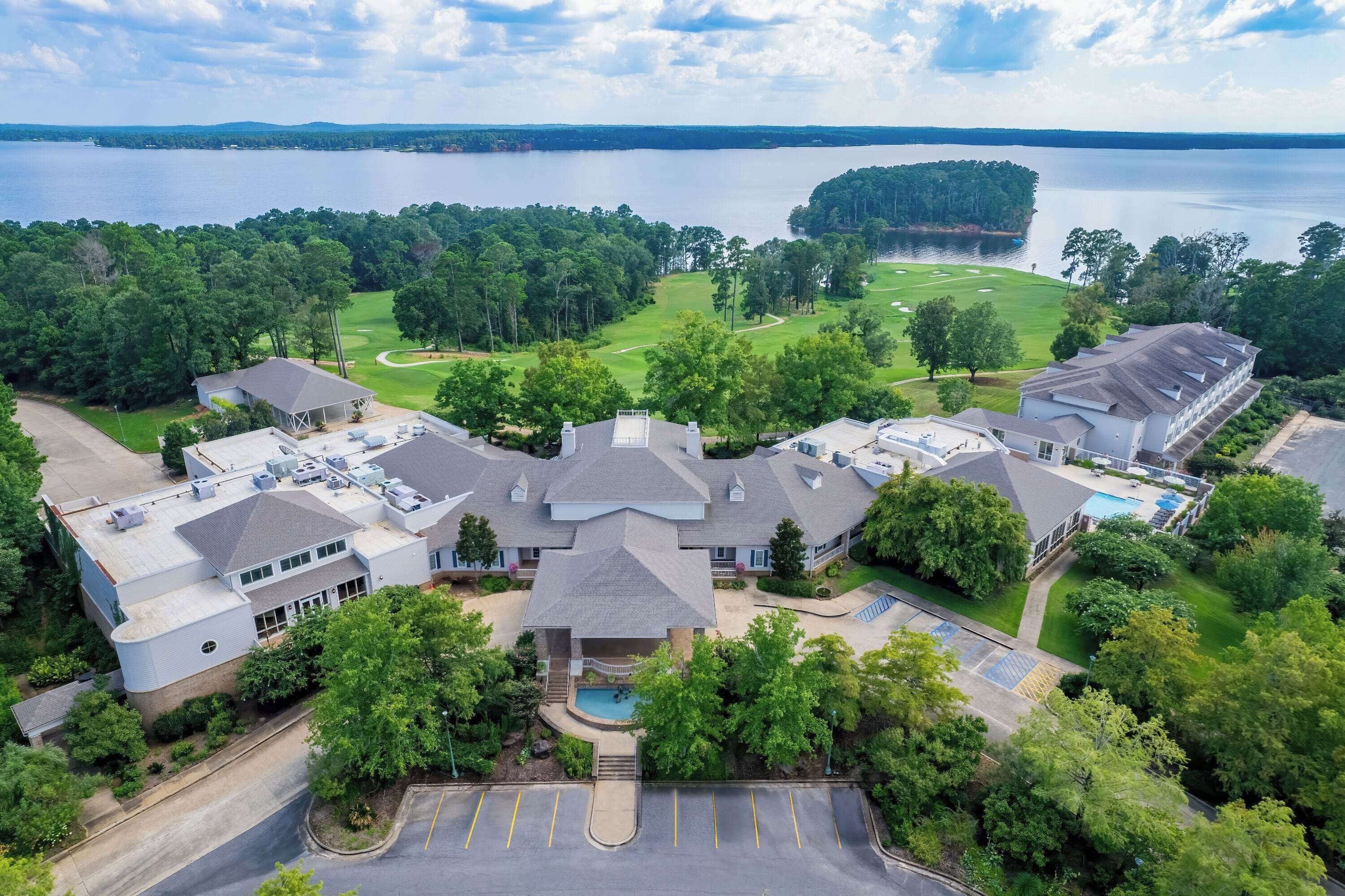 A large hotel with multiple buildings, a swimming pool, and a golf course in the background.