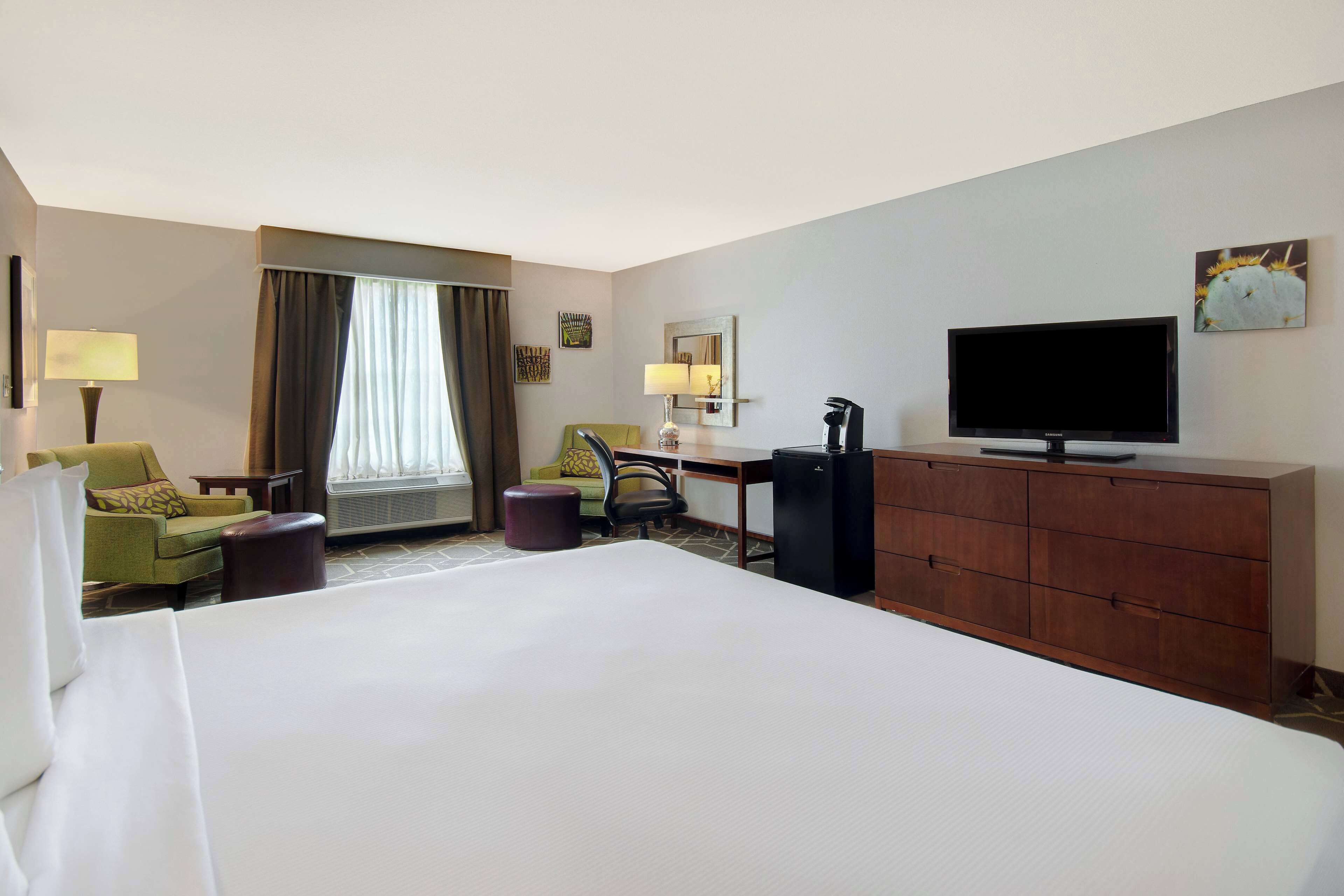A hotel room with a large bed, a desk with a chair, a television, and a window with curtains.
