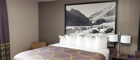 A hotel room with a bed, a nightstand with a lamp, and a large framed picture of a mountainous landscape.