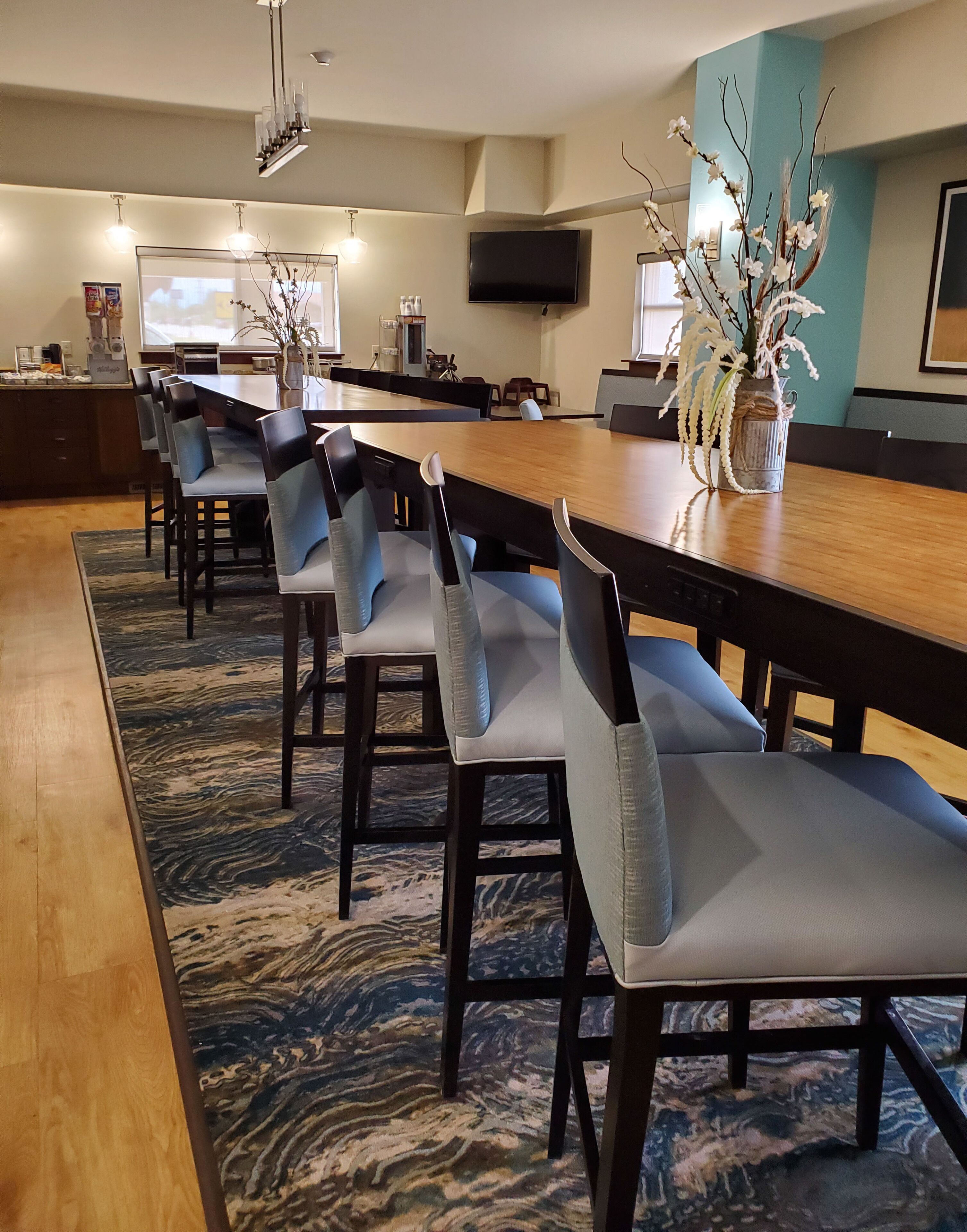 A modern dining area with a long wooden table, multiple chairs, and a decorative vase with branches.