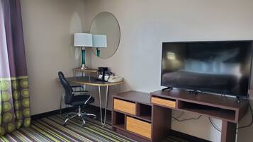 A hotel room with a bed, a TV, a desk with a lamp, a chair, and a striped carpet.