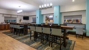 A modern dining area with a long table and chairs, a kitchen area with a TV, and a seating area with a bench.