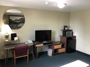 A hotel room with a desk, chair, TV, microwave, and a trash bin.