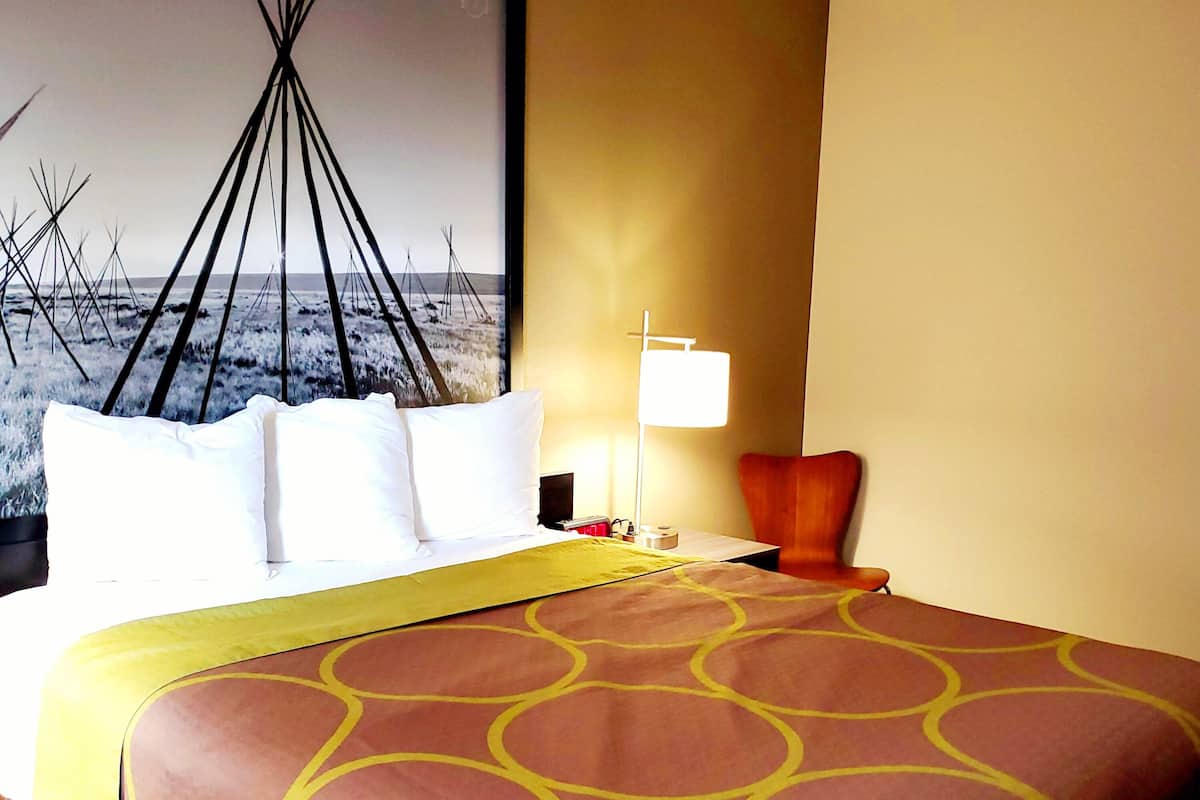 Ett hotellrum med en stor säng, ett nattduksbord, en lampa och en väggdekoration som föreställer ett tipi-tält.