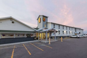 A hotel with a covered entrance, a parking lot, and a building with a sign on the roof.